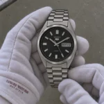 Seiko 5 SNXS79K1 automatic watch in white gloves under subdued room lighting — illustrative image